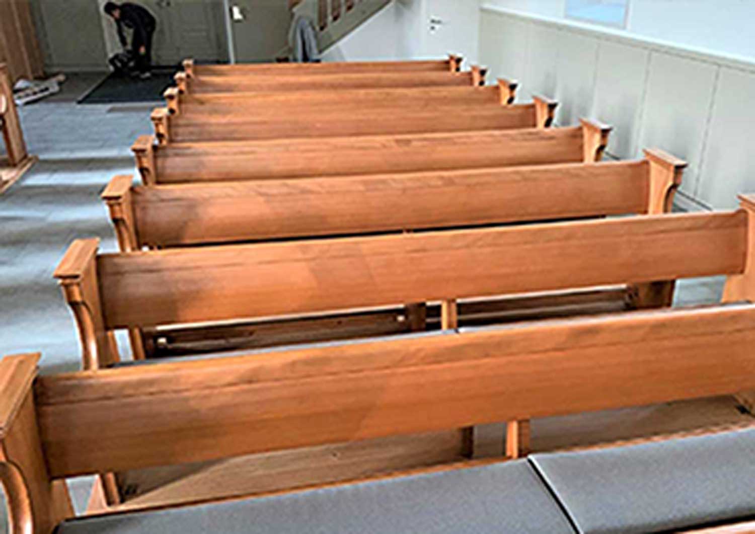 Holzbankreihen in einer Kirche, ein Mann steht in der Mitte.